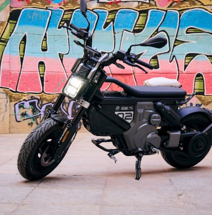 <p>ALT de la imagen: BMW CE 02 estacionada con conudctores sosteniéndola.</p>